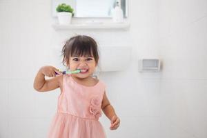 niñita linda limpiándose los dientes con cepillo de dientes en el baño foto