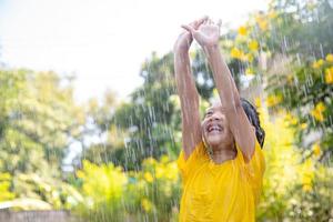 Happy Asian little child girl having fun to play with the rain in the sunlight photo