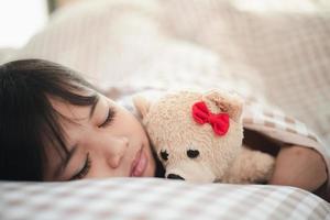 child little girl sleeps in the bed with a toy teddy bear photo