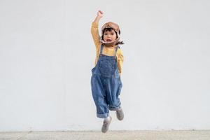 sueños de vuelo niña pequeña jugando con un sombrero de piloto sobre fondo blanco foto