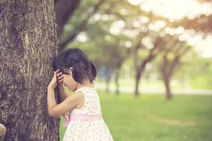 la niña está jugando al escondite escondiendo la cara en el parque.color vintage foto