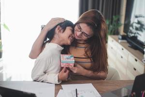 Happy Mother's day. Young woman mom getting congratulations from excited cute little daughter at home, child giving mother gift box while she working on laptop. Family holidays concept photo