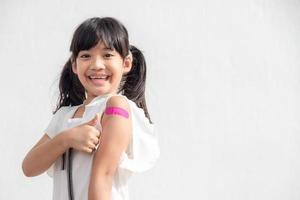 Asian little girl showing his arm after got vaccinated or inoculation, child immunization, covid delta vaccine concept photo