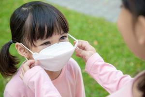 Concept of preventing a coronavirus covid-19 and viral infections. Mother puts on a medical mask for little girl before leaving home for school photo