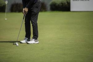 Golf player at the putting green hitting ball into a hole photo