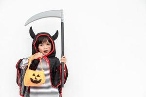 Children girl wearing mysterious Halloween dress holding a scary pumpkin and sickle. photo