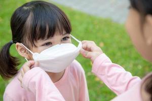 Concept of preventing a coronavirus covid-19 and viral infections. Mother puts on a medical mask for little girl before leaving home for school photo