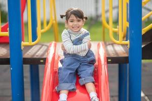 Asian Child girl playing on the outdoor playground. Kids play in school or kindergarten yard. Healthy summer activity for children. photo