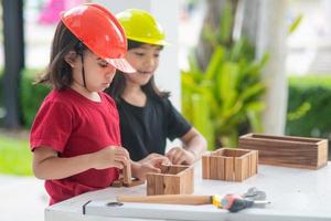 hermanos asiáticos niñas con sombreros de ingeniería construyendo casa con el juguete de madera. para aprender y mejorar el desarrollo, pequeño arquitecto. foto