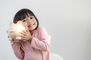 Little Asian girl saving money in a piggy bank, learning about saving, Kid save money for future education. Money, finances, insurance, and people concept photo