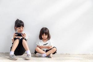 concepto de niños y artilugios. dos niñas hermanos hermanas miran el teléfono y sonríen. sostienen un teléfono inteligente, ven videos, aprenden, juegan, hablan en línea. Internet para niños. control parental foto