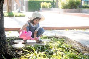 niña asiática vertiendo agua en los árboles. niño ayuda a cuidar las plantas con una regadera en el jardín. foto