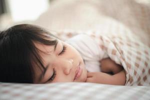 niña pequeña duerme en la cama con un oso de peluche de juguete foto