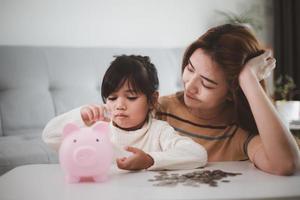 madre e hija poniendo monedas en la alcancía. presupuesto familiar y concepto de ahorro. concepto de cuenta de ahorro junior foto