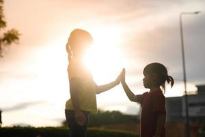 linda niña asiática haciendo gesto de hola cinco y puesta de sol foto