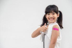 Asian little girl showing his arm after got vaccinated or inoculation, child immunization, covid delta vaccine concept photo