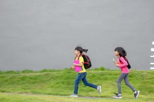 De vuelta a la escuela. dos lindas niñas asiáticas con mochila escolar sosteniendo un libro y caminando juntas en la escuela foto