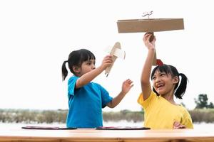 dos niños pequeños jugando con un avión de juguete de cartón en el parque durante el día. concepto de juego feliz. niño divirtiéndose al aire libre. foto