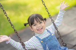 niña asiática feliz jugando al columpio al aire libre en el parque foto