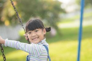 Happy little Asian girl playing swing outdoor in the park photo