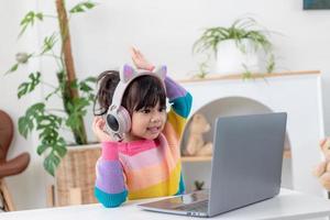 Smiling little Asian girl have a video call distant class with teacher using laptop, social distance during quarantine isolation during the Coronavirus photo