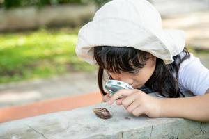 Happy kid girl exploring nature with a magnifying glass and a snail. He having fun in the garden. The concept of the kid is ready to go to school. photo