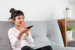 Kid with remote control sitting on the couch watching a movie on tv photo