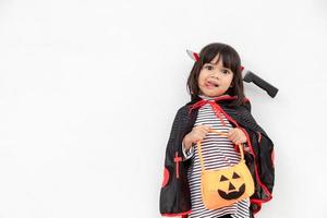 divertido concepto de niño de halloween, niña linda con disfraz de fantasma de halloween aterrador que sostiene un fantasma de calabaza naranja en la mano, sobre fondo blanco foto