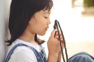 niña asiática rezando sosteniendo la cruz, concepto cristiano. foto