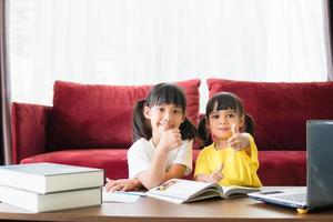 dos niñas estudiantes asiáticas estudian en línea con el maestro por videollamada juntas. los hermanos están educando en casa con una computadora portátil durante la cuarentena debido a la pandemia de covid 19. foto