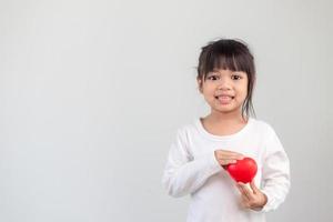 la niña con una camisa blanca sosteniendo un corazón rojo sobre un fondo blanco. tarjetas de felicitación para el día de san valentín, día de la madre, día del padre. foto