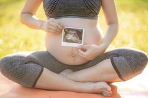 Pregnant woman holding ultrasound photo near her pregnant belly