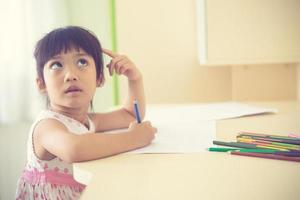 Little Asian child using a pencil to write on notebook at the desk photo