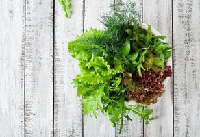 Variety fresh organic herbs lettuce, arugula, dill, mint, red lettuce on wooden background in rustic style