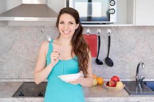 Young healthy laughing caucasian woman has breakfast, holds a plate and a spoon photo