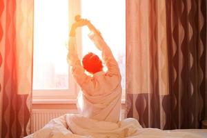 Back view caucasian woman stretching arms and body near window after waking up photo