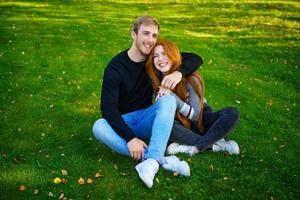 feliz pareja joven sentada en un abrazo en el parque en el césped foto