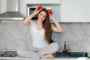 la mujer en la cocina se sienta en la mesa, la niña sostiene manzanas junto a su cabeza en lugar de ella foto