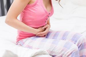 Unhealthy woman sitting on bed touching her stomach suffering from more photo