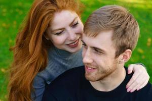 feliz pareja joven sentada en un abrazo en el parque en el césped foto