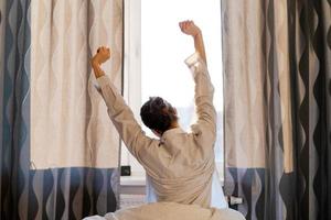 Back view caucasian woman stretching arms and body near window after waking up photo