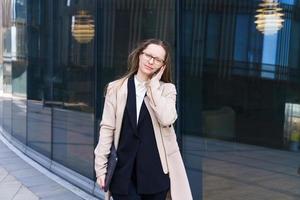 gafas de mujer de negocios con laptop sus manos hablando por teléfono cerca del centro de negocios foto