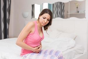 Unhealthy woman sitting on bed touching her stomach suffering from more photo