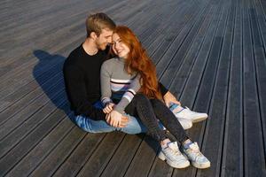 feliz pareja chico y chica están sentados en una terraza de madera abrazándose foto