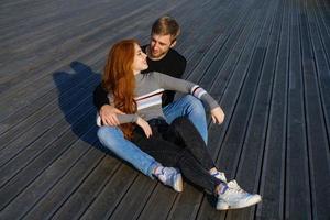 una pareja joven está sentada en el parque en un banco de madera abrazándose foto