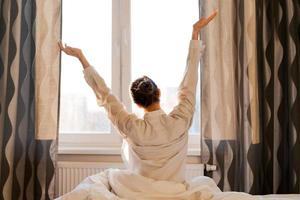 Back view caucasian woman stretching arms and body near window after waking up photo