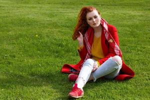 lonely woman in red coat sits on green grass photo