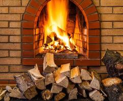 stack of firewood and fire in brick fireplace photo