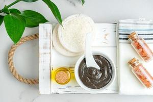 Top view of a bowl with handmade clay mask enriched with natural essential oil on wooden tray. Spa procedures at home. photo