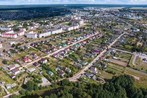 aerial panoramic view of green village with houses, barns and gravel road in forest photo
